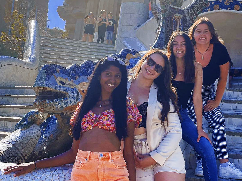 A diverse group of female HPAO students in Spain. It is sunny and they are on a patio with elaborate mosaics and tiled statues and steps.